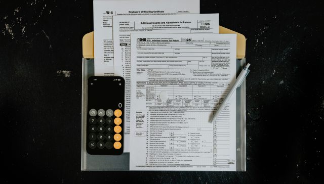 Tax forms, calculator, and a pen on a desk representing cross-border financial services and financial planning.
