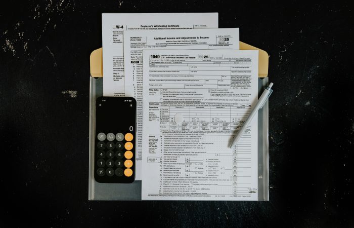 Tax forms, calculator, and a pen on a desk representing cross-border financial services and financial planning.