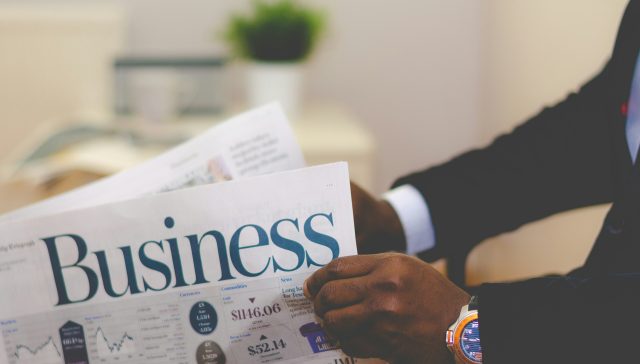Professional reading a business newspaper with market data and financial charts