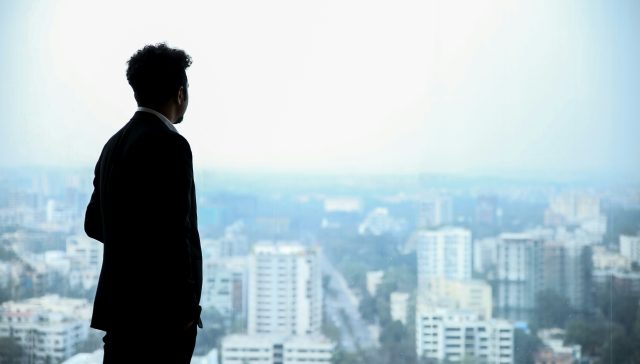 A corporate executive in a suit looking out over a city skyline, representing business leaders exploring O-1A, EB-1A, and EB-2 NIW immigration pathways.